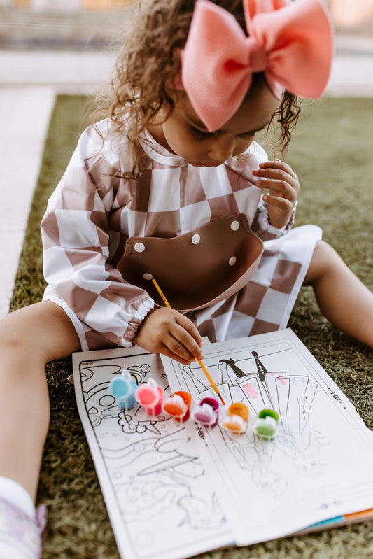 Concentrated toddler coloring with paint while wearing a Bibvy olive green and white checkered bib, perfect for messy playtime activities