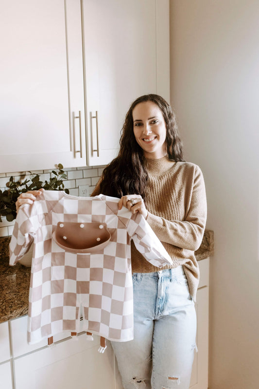 Danielle, founder of Bibvy, holding an mauve pink and white checkered bib in a bright, modern kitchen.
