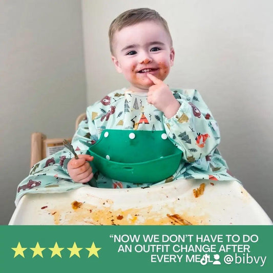 A smiling toddler with a face full of food in a high chair, wearing a Bibvy bib. The quote says 'Now we don’t have to do an outfit change after every meal! @bibvy' with five stars below.