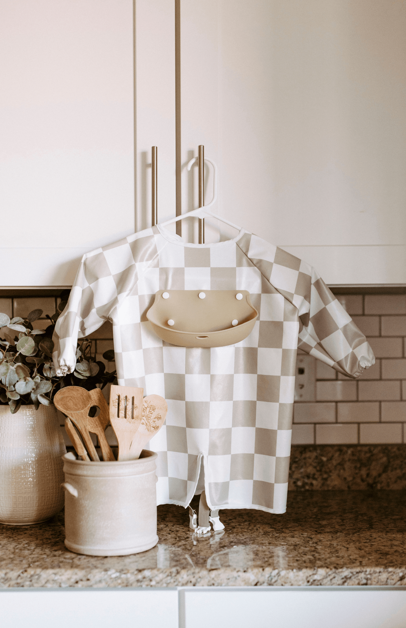 Olive green and white checkered Bibvy bib displayed in a kitchen, showcasing the front silicone food catcher.